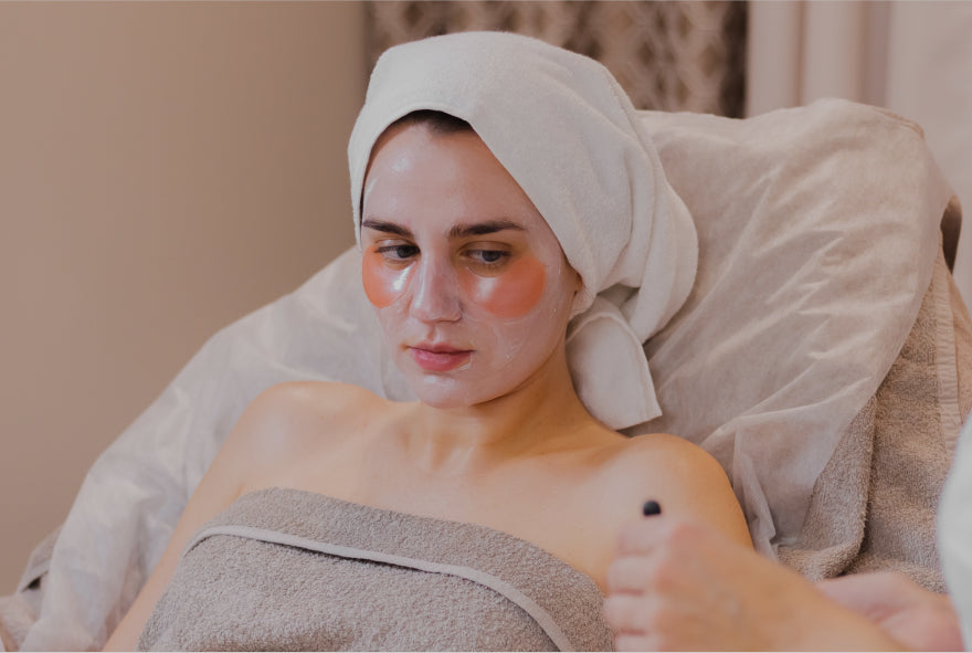 Woman with a towel on her head and face mask, sitting in a chair.