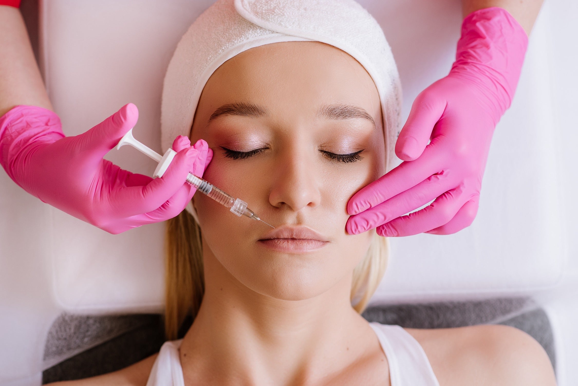 Woman receiving facial fillertreatment with pink gloves 
