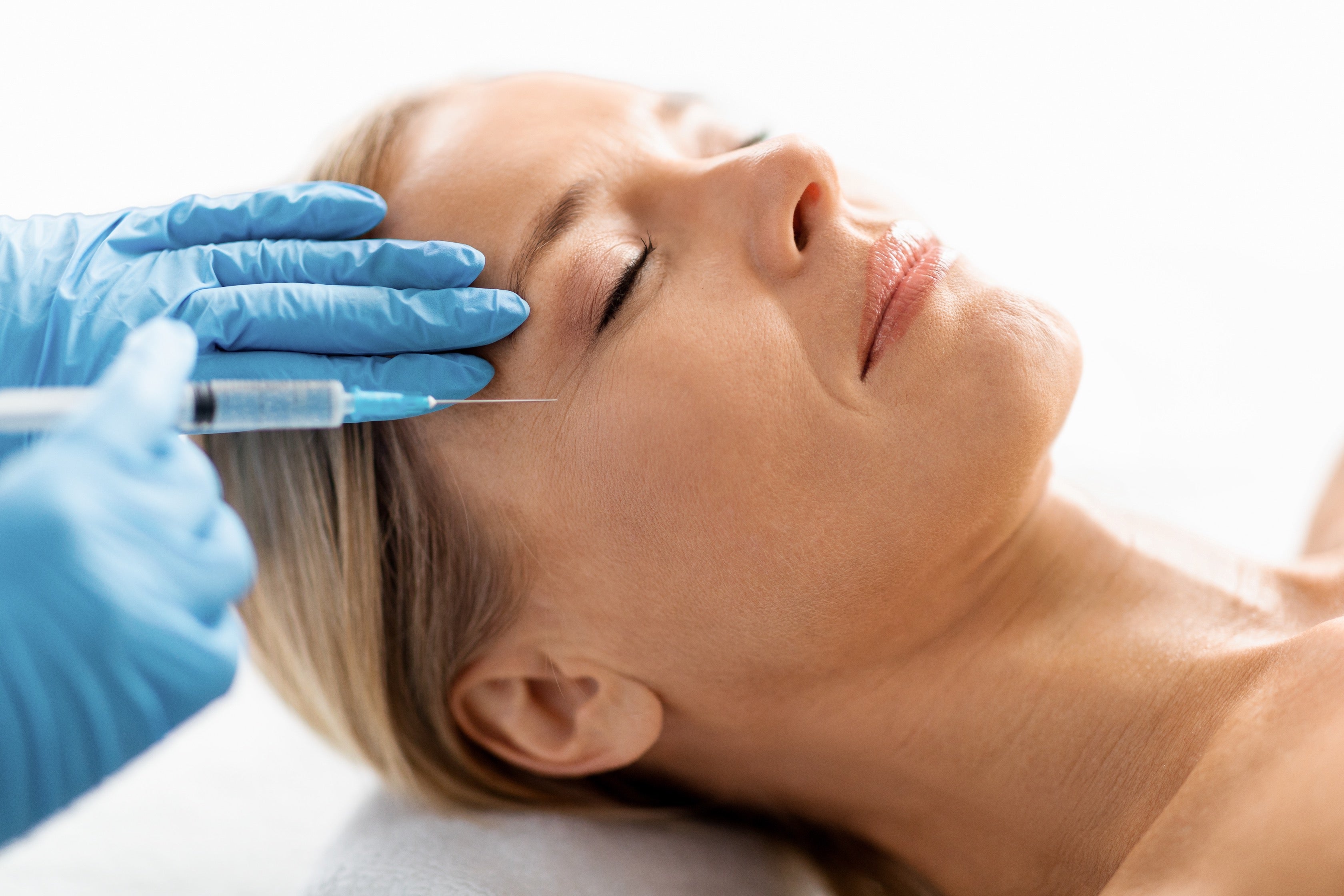 Woman receiving facial injection treatment with blue gloves on a white background