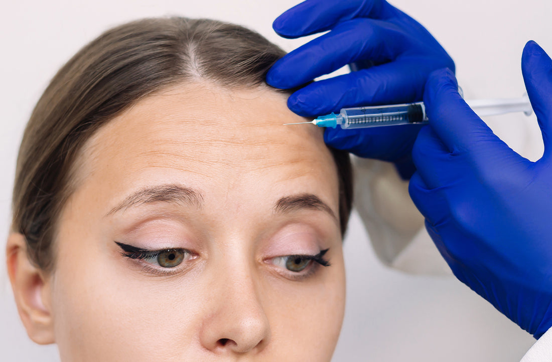 Person receiving a facial injection with blue gloves on a neutral background