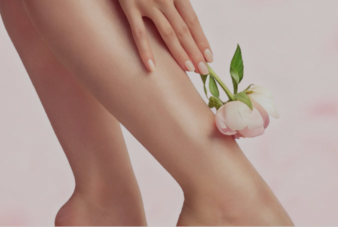 Close-up of a clean & hairless woman's leg with a hand holding a small flower against a pink background