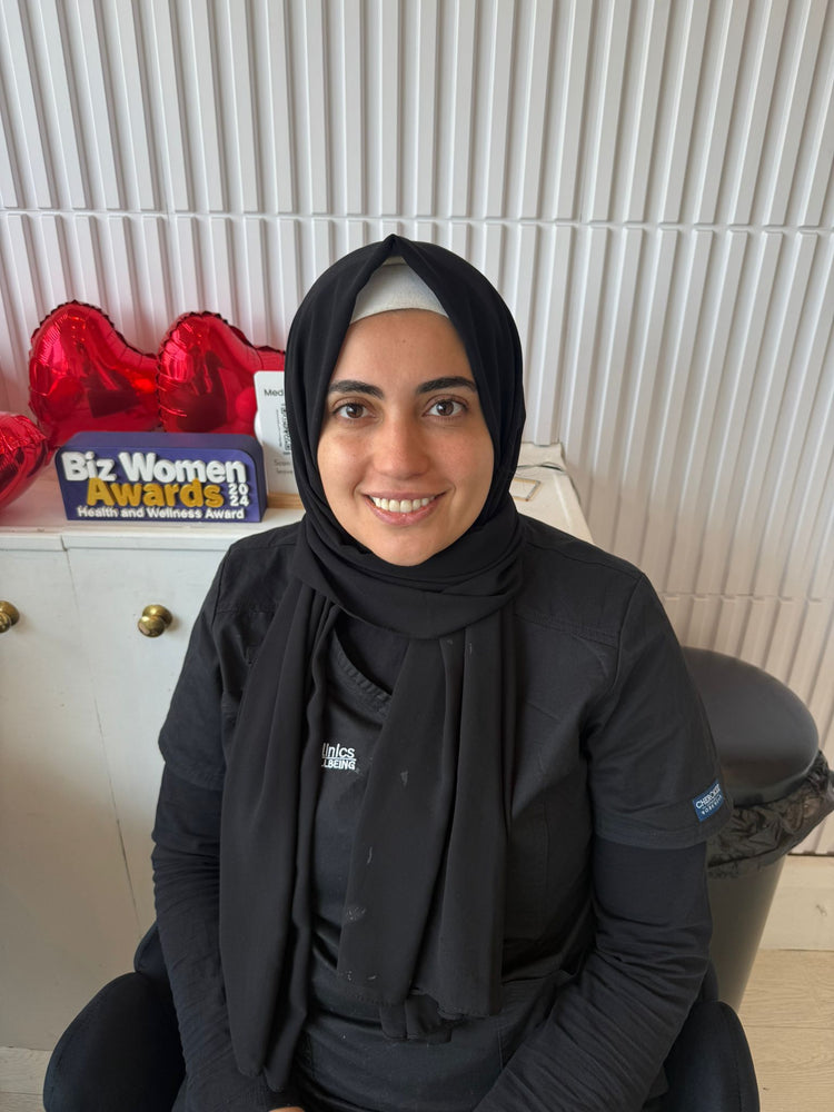Woman wearing a black hijab sitting in front of a shelf with decorative items and an award box.